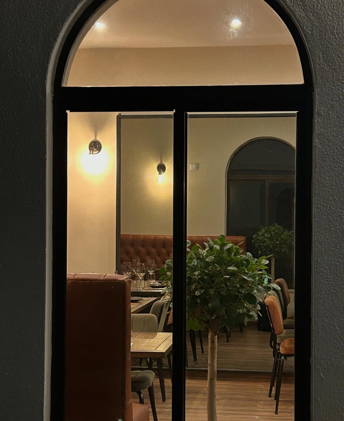 Entrada em arco do Maria Petisca à noite, com a sala iluminada e uma árvore junto à porta